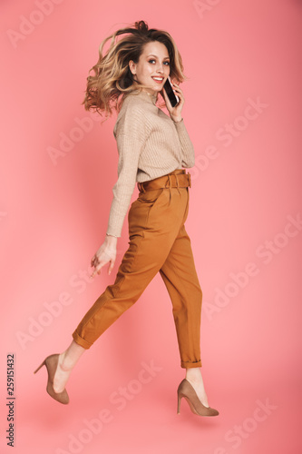 Full length portrait of pretty woman smiling and walking isolated over pink background
