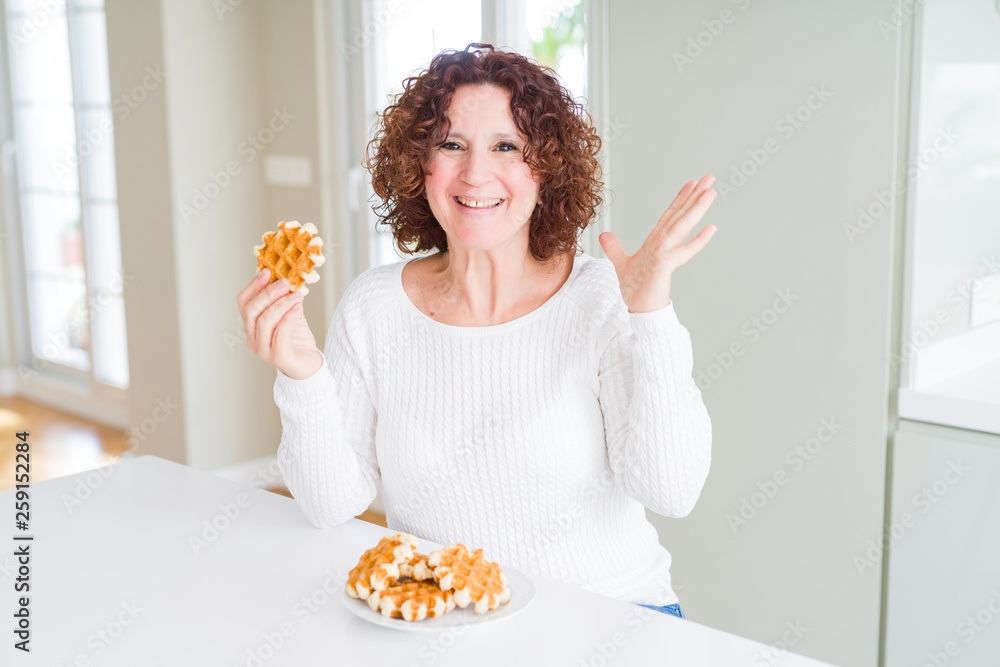Senior woman eating sweet belgian waffle very happy and excited, winner expression celebrating victory screaming with big smile and raised hands Senior woman eating sweet belgian waffle very happy and excited, winner expression celebrating victory screaming with big smile and raised hands
