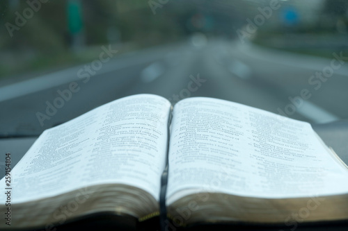 Open Holy Bible nside the car. Background blurred with desert highway. Close-up. Horizontal shot.