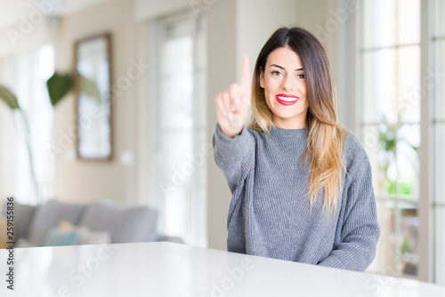 Free Download Young beautiful woman wearing winter sweater at home showing and pointing up with finger number one while smiling confident and happy. - GFXLoad