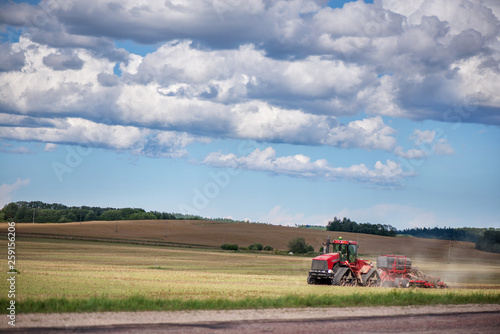 Agricultural background with red tractor pulling plow, throwing dust in air. Combine harvester at wheat field. Heavy machinery during cultivation, working on fields. Dramatic sky, rain, storm clouds
