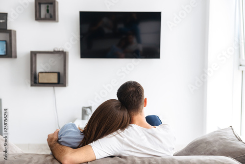 Image from back of happy couple watching television on sofa at home