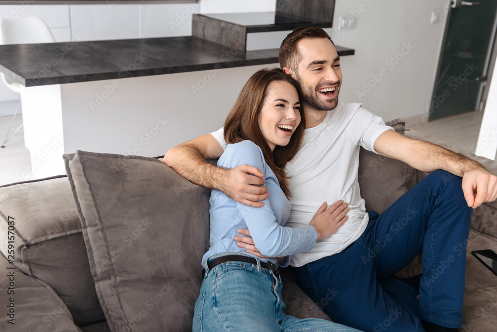 Image of satisfied couple hugging together at home while sitting on sofa Image of satisfied couple hugging together at home while sitting on sofa