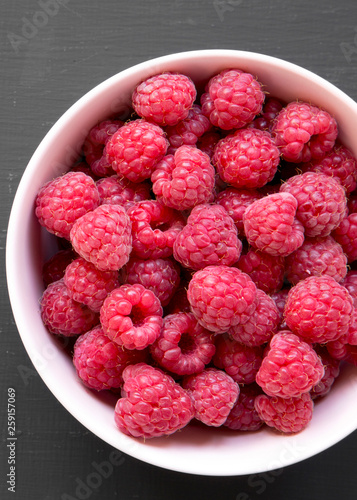 Raspberry in a pink bowl over black surface, overhead view. From above, top view, flat lay. Close-up.