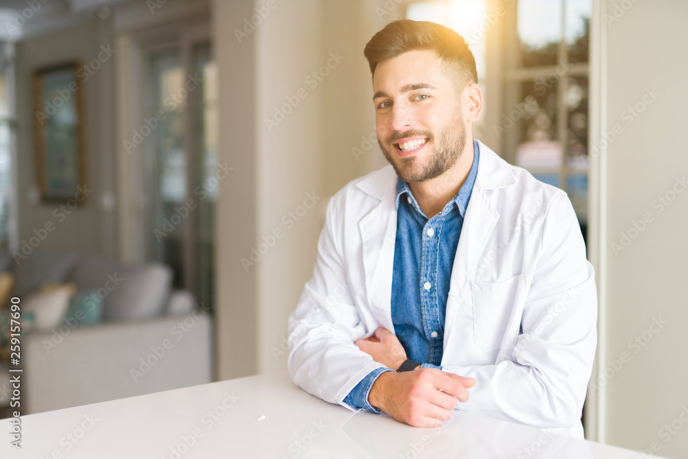 Young handsome doctor man at the clinic looking away to side with smile on face, natural expression. Laughing confident.