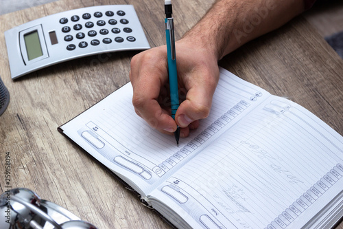 Man writing in to notebook reminder daily agenda for coming month,year,week. Daily business, routine planning. Time management.