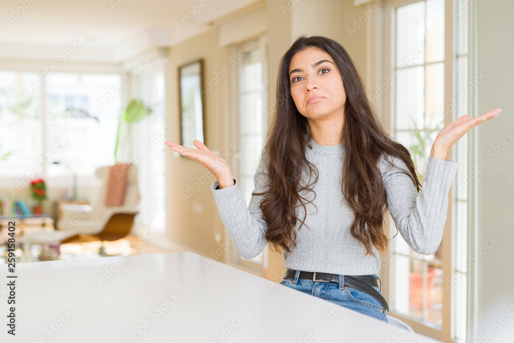 Young beautiful woman at home clueless and confused expression with arms and hands raised. Doubt concept. Young beautiful woman at home clueless and confused expression with arms and hands raised. Doubt concept.