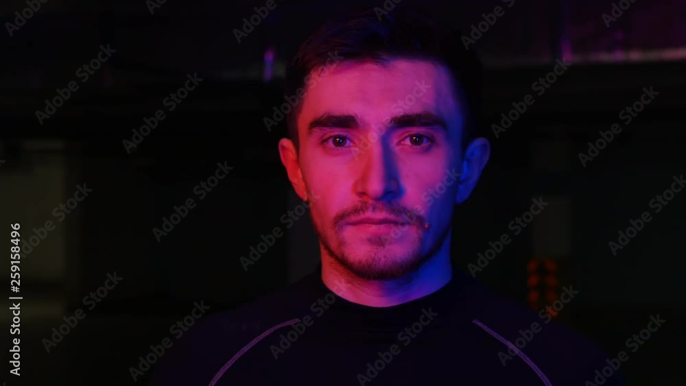 A young man on the underground parking coming from the dark in neon lighting A young man on the underground parking coming from the dark in neon lighting