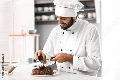 Male confectioner decorating tasty chocolate cake in kitchen
