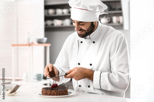 Male confectioner decorating tasty chocolate cake in kitchen photo