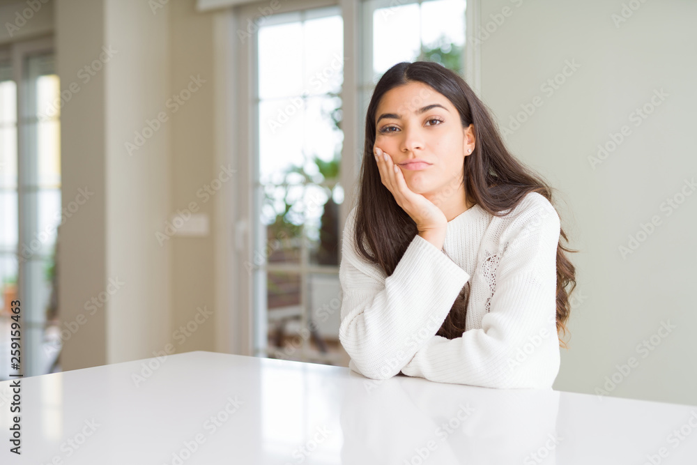 Young beautiful woman at home on white table thinking looking tired and bored with depression problems with crossed arms. Young beautiful woman at home on white table thinking looking tired and bored with depression problems with crossed arms.