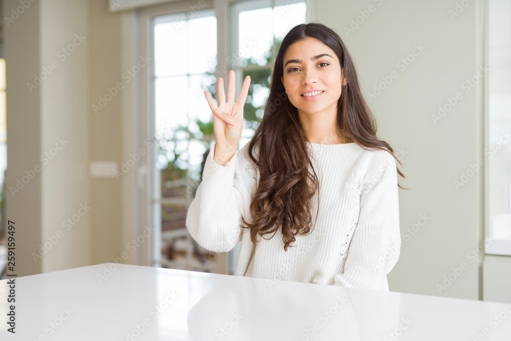 Young beautiful woman at home on white table showing and pointing up with fingers number four while smiling confident and happy. Young beautiful woman at home on white table showing and pointing up with fingers number four while smiling confident and happy.