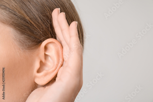 Young woman with hearing problem on light background, closeup photo
