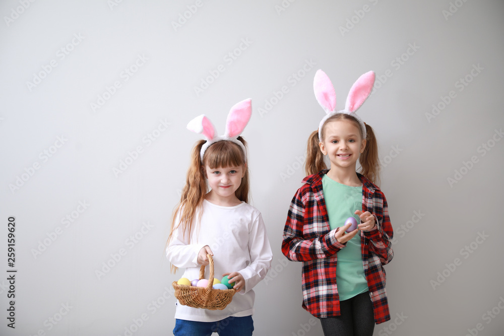 Cute little children with Easter eggs and bunny ears on light background