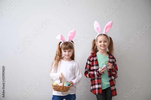 Cute little children with Easter eggs and bunny ears on light background