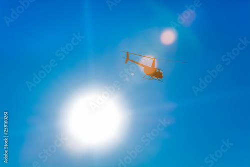 Silhouette of helicopter in blue clear sky with solar patches of light. Warm spring day. Modern transport.