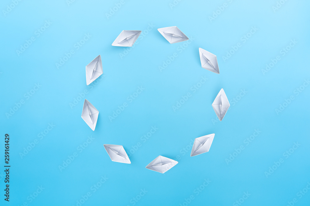 White paper ships float in a circle on blue background