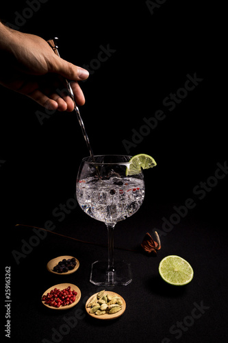barman preparing a gin and tonic cocktail on a black background next to his ingredients