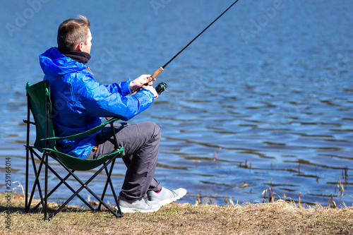 Fisherman sitting in chair with fishing rod catching fish on lakeside.