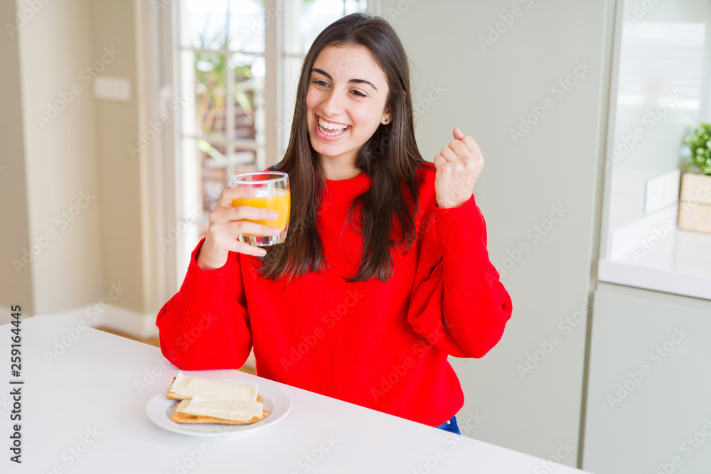 Beautiful young woman eating toasts and orange juice for snack or breakfast screaming proud and celebrating victory and success very excited, cheering emotion Beautiful young woman eating toasts and orange juice for snack or breakfast screaming proud and celebrating victory and success very excited, cheering emotion