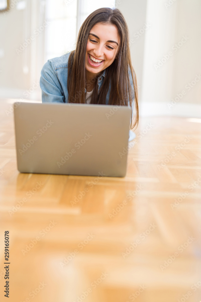 Beautiful young woman laying on the floor using laptop with a happy face standing and smiling with a confident smile showing teeth Beautiful young woman laying on the floor using laptop with a happy face standing and smiling with a confident smile showing teeth
