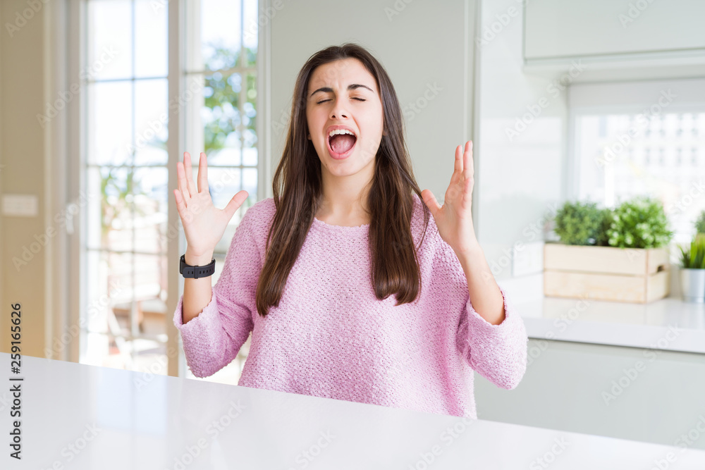 Beautiful young woman wearing pink sweater crazy and mad shouting and yelling with aggressive expression and arms raised. Frustration concept.