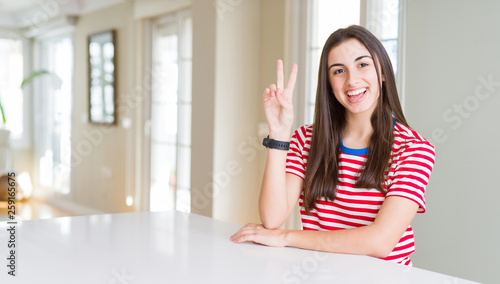 Beautiful young woman wearing casual stripes t-shirt smiling with happy face winking at the camera doing victory sign. Number two.