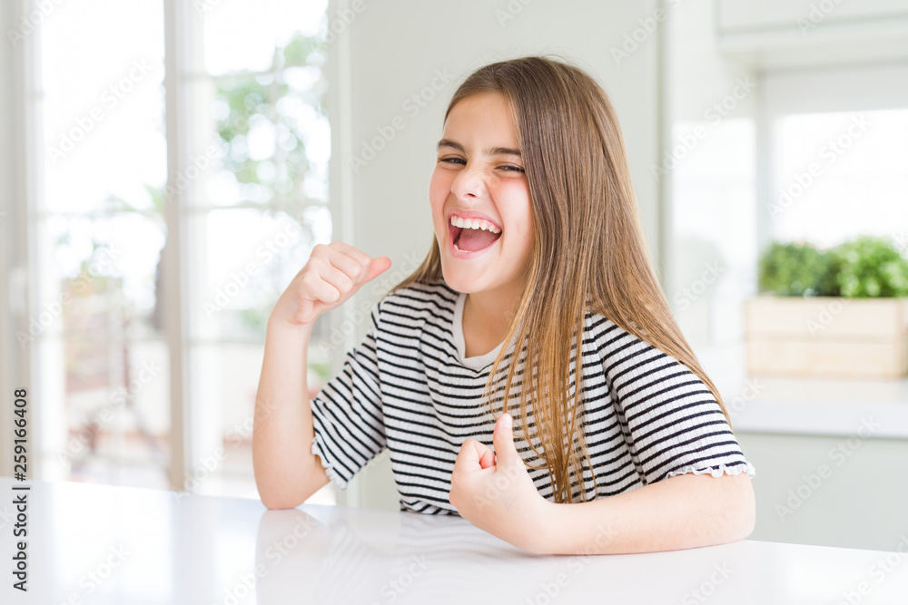 Beautiful young girl kid wearing stripes t-shirt very happy and excited doing winner gesture with arms raised, smiling and screaming for success. Celebration concept.