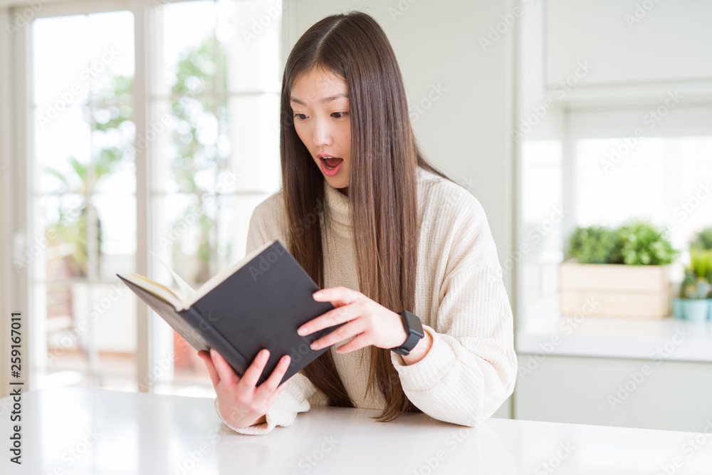 Beautiful Asian woman reading a book scared in shock with a surprise face, afraid and excited with fear expression Beautiful Asian woman reading a book scared in shock with a surprise face, afraid and excited with fear expression