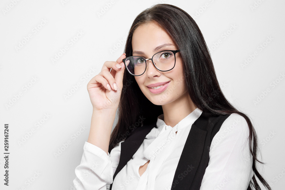 A young beautiful smart woman in a black suit and white blouse is standing on a white background with arms crossed. Competent serious employee managing. Concept of business woman, the head.