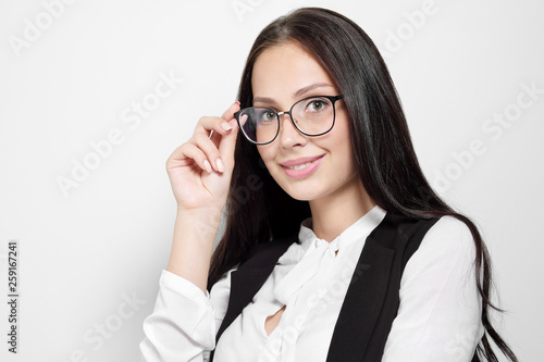 A young beautiful smart woman in a black suit and white blouse is standing on a white background with arms crossed. Competent serious employee managing. Concept of business woman, the head.