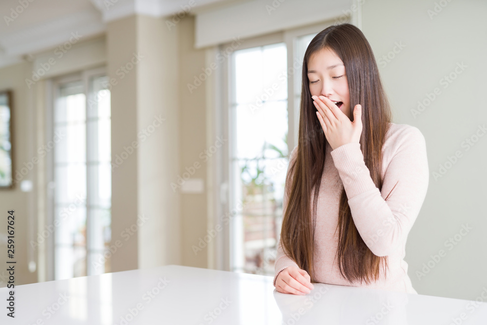 Beautiful Asian woman wearing casual sweater on white table bored yawning tired covering mouth with hand. Restless and sleepiness. Beautiful Asian woman wearing casual sweater on white table bored yawning tired covering mouth with hand. Restless and sleepiness.