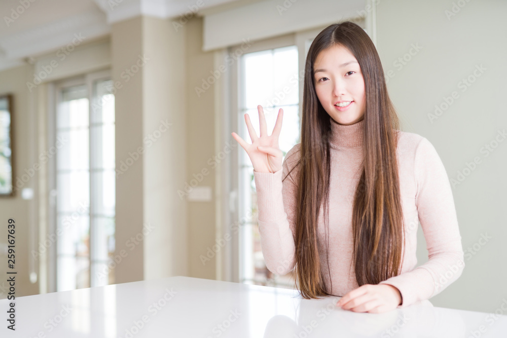 Beautiful Asian woman wearing casual sweater on white table showing and pointing up with fingers number four while smiling confident and happy. Beautiful Asian woman wearing casual sweater on white table showing and pointing up with fingers number four while smiling confident and happy.