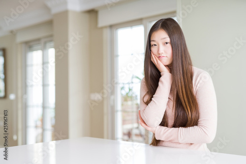 Beautiful Asian woman wearing casual sweater on white table thinking looking tired and bored with depression problems with crossed arms.