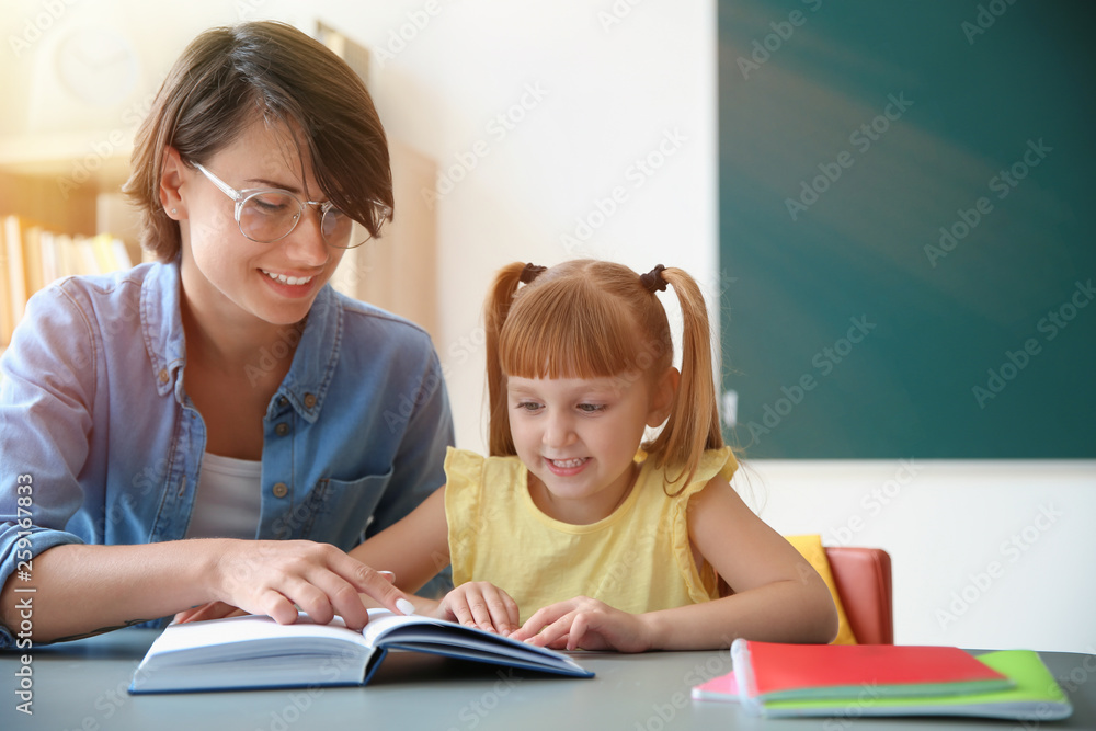 Teacher with pupil reading book at table in classroom, space for text Teacher with pupil reading book at table in classroom, space for text