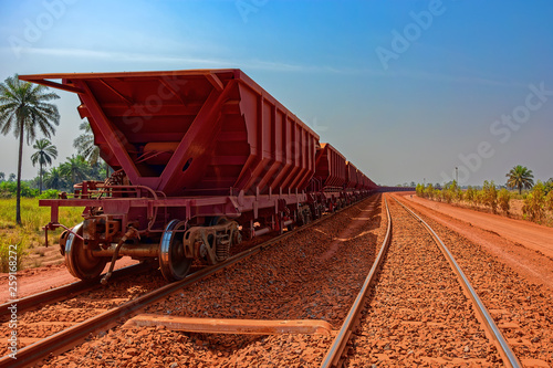 A freight train carrying bauxite in railway carriages for transhipment into a capesize bulk carrier ships by covered conveyor belt mechanism in the Kamsar, Guinea, Africa.