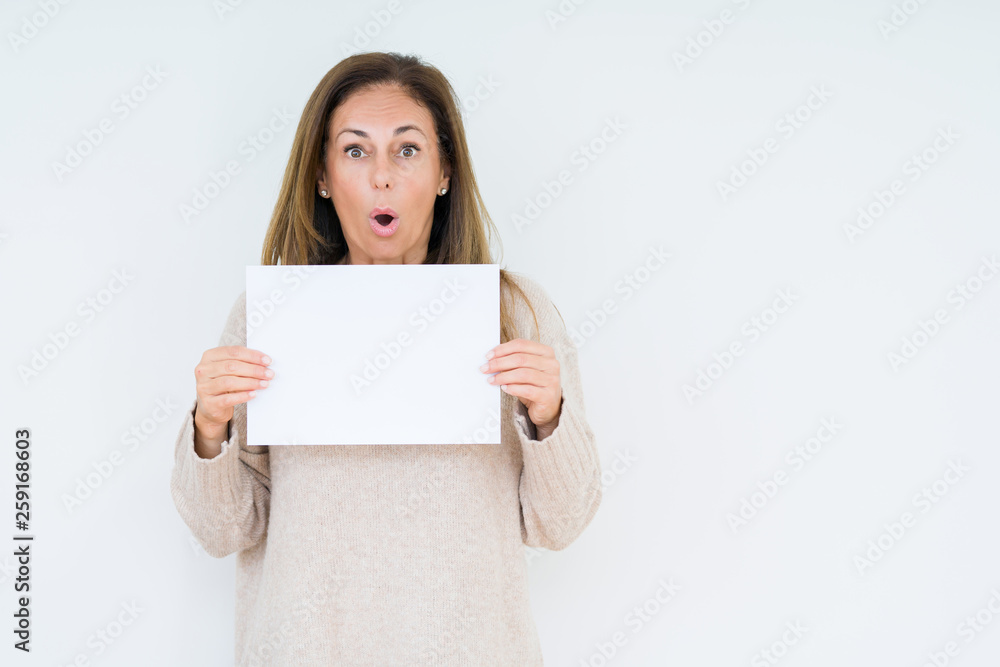 Middle age woman holding blank paper sheet over isolated background scared in shock with a surprise face, afraid and excited with fear expression Middle age woman holding blank paper sheet over isolated background scared in shock with a surprise face, afraid and excited with fear expression
