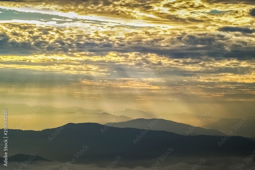 Mountain view morning of many hills cover with yellow sun rays in the sky background, sunrise at Doi Samur Dao, Sri Nan National Park, Nan, Thailand.