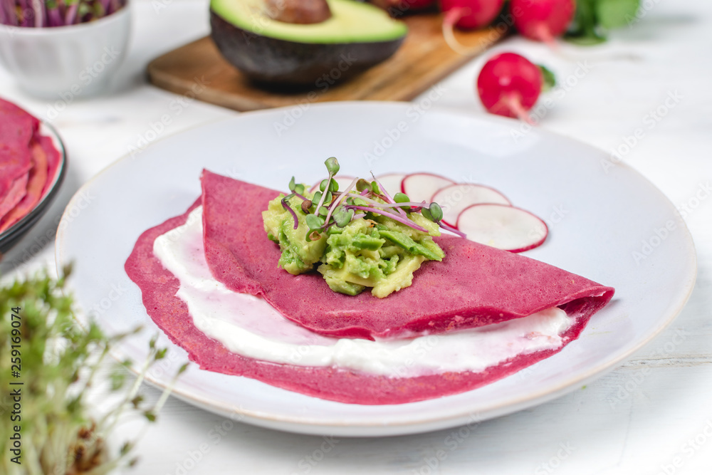 Tasty appetizing beetroot pancakes served on plate with avocado, sprouts and pink radish, white wooden table