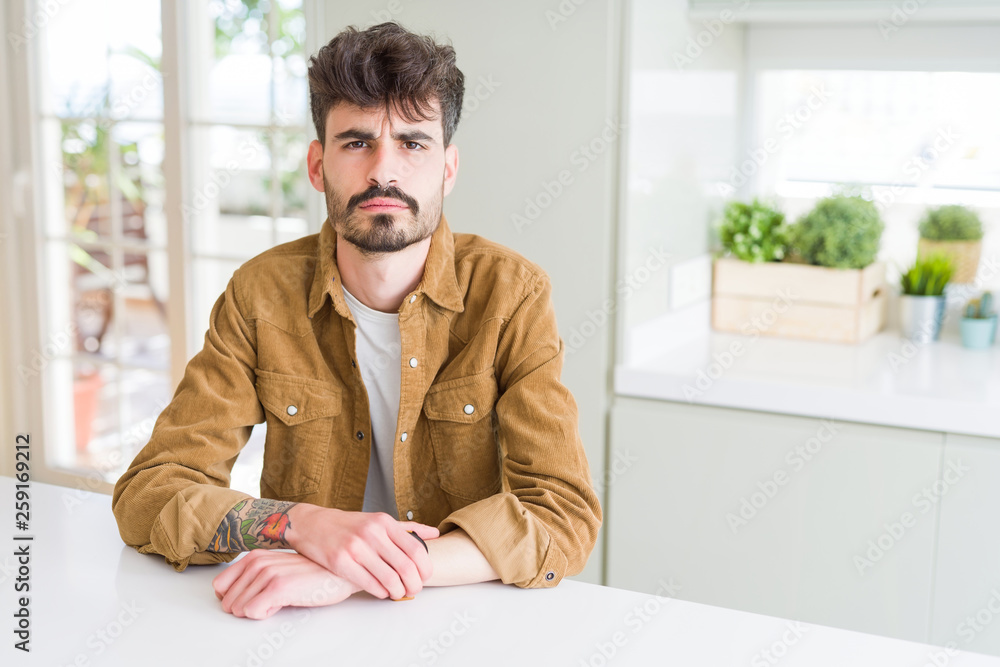 Young man wearing casual jacket sitting on white table skeptic and nervous, frowning upset because of problem. Negative person. Young man wearing casual jacket sitting on white table skeptic and nervous, frowning upset because of problem. Negative person.