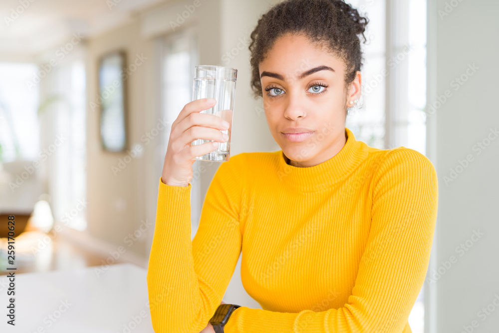 Young african american woman drinking a glass of fresh water with a confident expression on smart face thinking serious Young african american woman drinking a glass of fresh water with a confident expression on smart face thinking serious