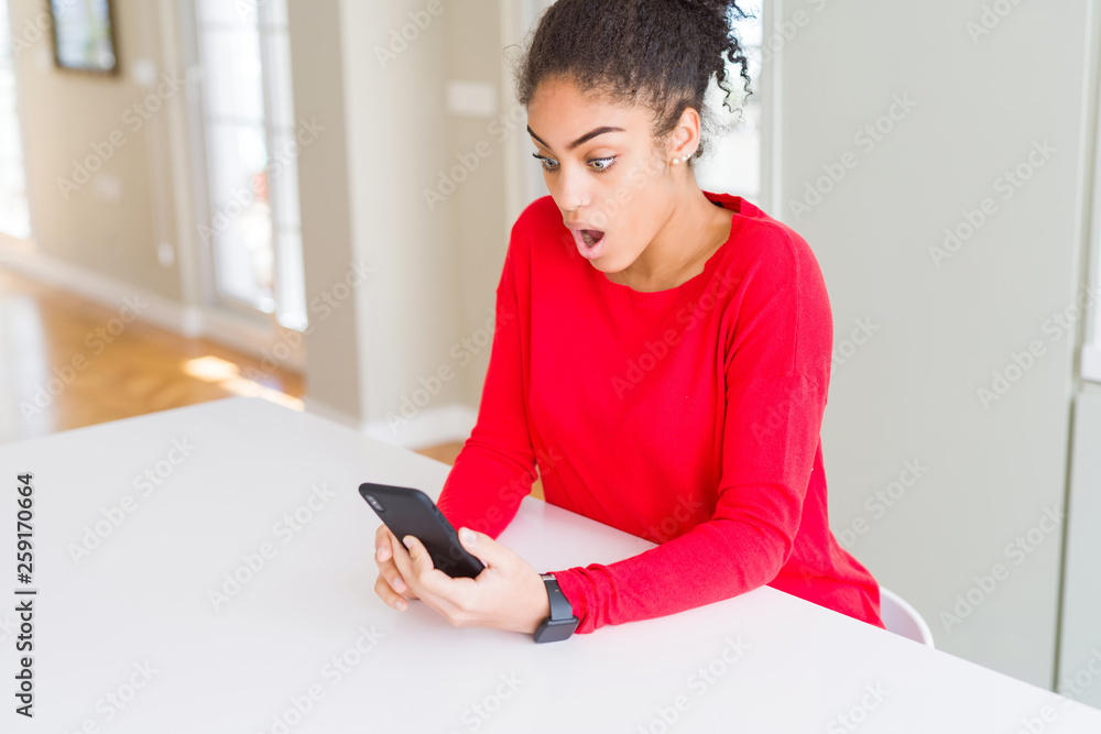 Young african american woman using smartphone texting a message scared in shock with a surprise face, afraid and excited with fear expression Young african american woman using smartphone texting a message scared in shock with a surprise face, afraid and excited with fear expression