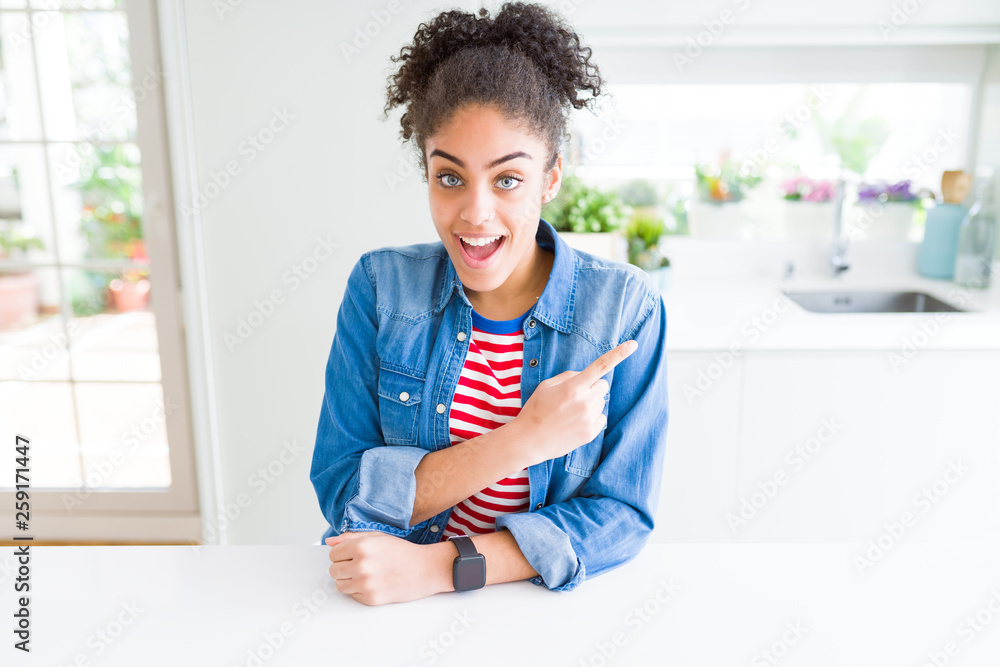 Beautiful young african american woman with afro hair wearing casual denim jacket cheerful with a smile of face pointing with hand and finger up to the side with happy and natural expression on face Beautiful young african american woman with afro hair wearing casual denim jacket cheerful with a smile of face pointing with hand and finger up to the side with happy and natural expression on face