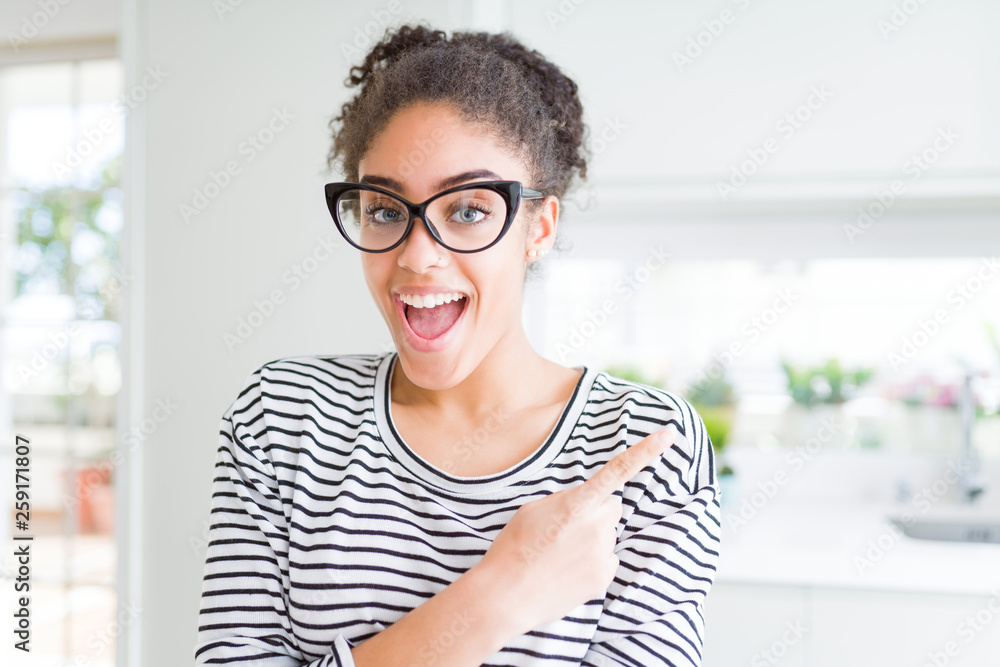 Beautiful young african american woman with afro hair wearing glasses cheerful with a smile of face pointing with hand and finger up to the side with happy and natural expression on face Beautiful young african american woman with afro hair wearing glasses cheerful with a smile of face pointing with hand and finger up to the side with happy and natural expression on face