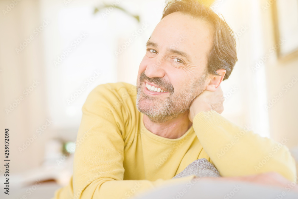 Handsome middle age man sitting on the sofa relaxed and smiling at the camera at home Handsome middle age man sitting on the sofa relaxed and smiling at the camera at home