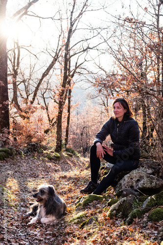 Woman with her dog in the forest enjoying sunset time.