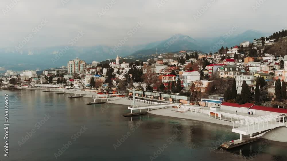 Aerial panoramic view of Yalta city embankment with sea in cloudy weather, mountains and breakwaters, beautiful resort for vacation, drone shot Aerial panoramic view of Yalta city embankment with sea in cloudy weather, mountains and breakwaters, beautiful resort for vacation, drone shot