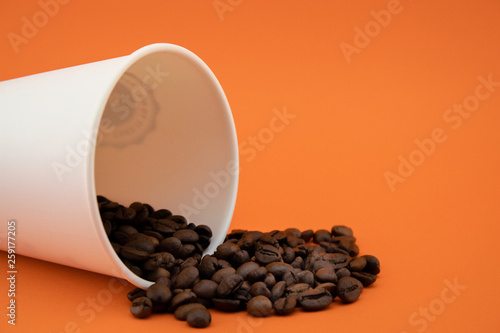 Take-out coffee cup with spilled coffee beans, orange background.