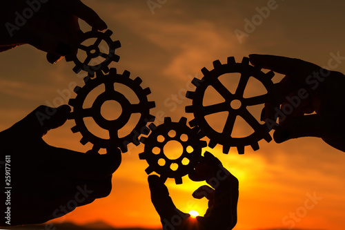 Gears in the hands of people on the background of the evening sky.  interaction, teamwork.