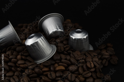 Espresso coffee capsules or coffee pods on coffee beans, black background.